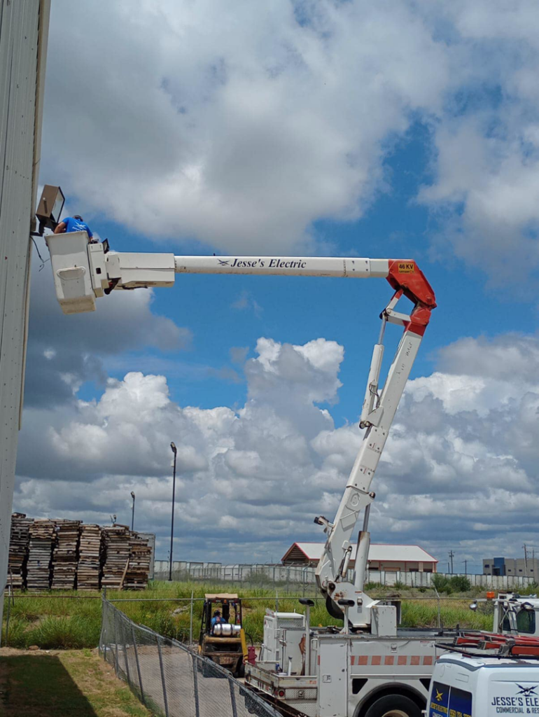 An electrician from Jesse's Electric repairing an outdoor light fixture from a bucket truck in Laredo, TX.