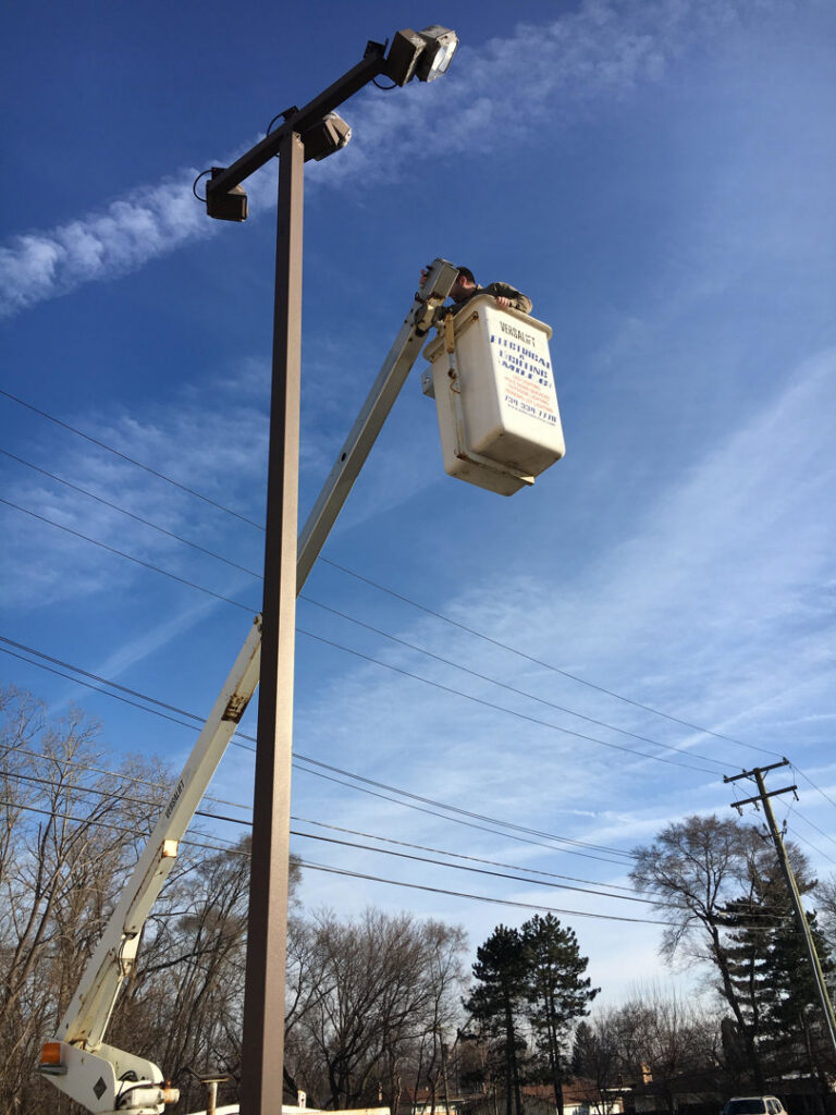An electrician from MDEC Electrical & Lighting in a bucket lift repairing an outdoor light pole in Livonia, MI.