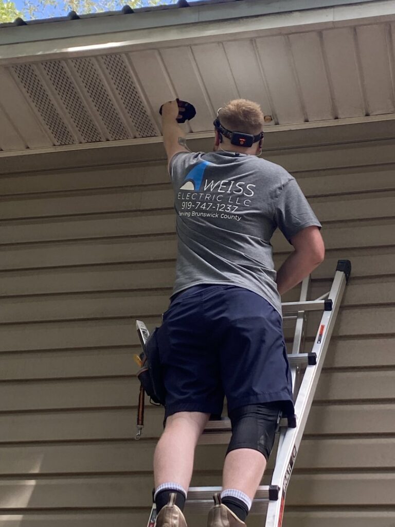 An electrician from Weiss Electric LLC on a ladder repairing an outdoor light fixture in Saint Charles, MO.