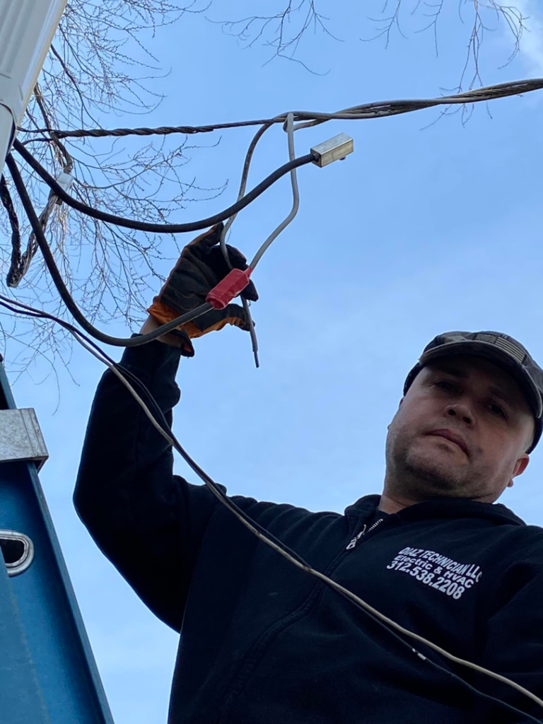 An electrician from Diaz Techician LLC in Chicago, IL, on a ladder repairing overhead electrical lines.