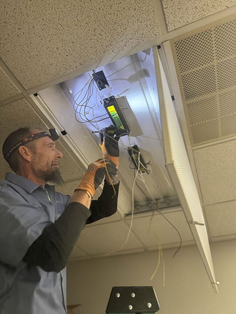 An electrician repairing an overhead light fixture with exposed wires at Three Rivers Electric in Fort Wayne, IN.
