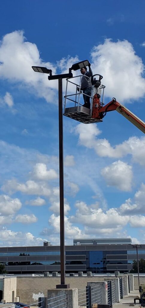 An electrician from Shark Electric in a boom lift repairing a parking lot light fixture in Houston, TX.