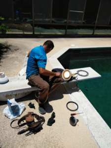 An electrician repairing or replacing a pool light fixture next to a swimming pool by Vazquez Electrical Contractor LLC in Dallas, TX