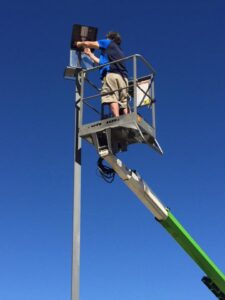 An electrician in a lift bucket repairing a street light against a clear blue sky for APEX Electrical Design in Fort Worth, TX