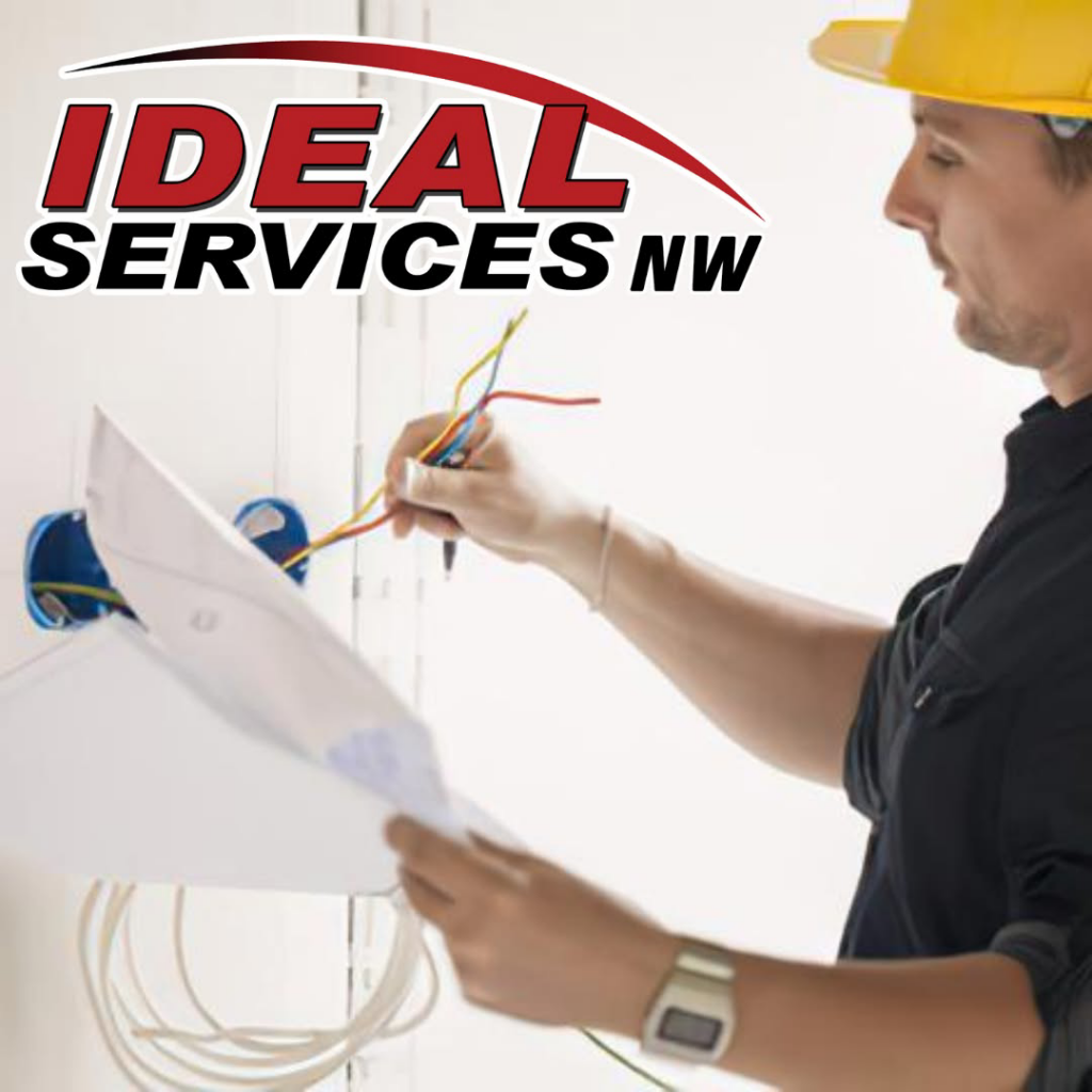 An electrician from Ideal Services NW in Fife, WA, reviewing blueprints while working on a wiring installation.