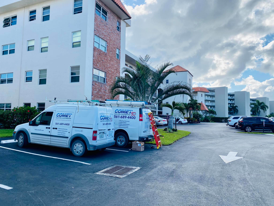 Two Comet Electric service vans with a ladder parked at a multi-story building for an electrician job in West Palm Beach, FL.