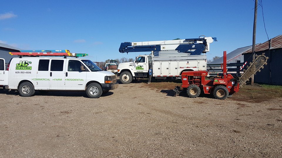 JC Electric, LLC service van, bucket truck, and trencher parked on a job site in Huron, SD.