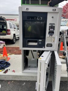 An electrician servicing an open ATM machine, likely for power installation or repair, by Peeler Electric Light & Power in Merrimack, NH.