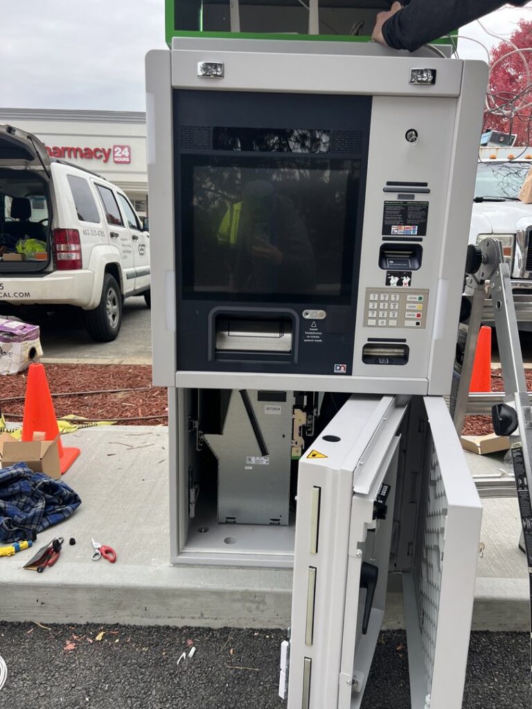 An electrician servicing an open ATM machine, likely for power installation or repair, by Peeler Electric Light & Power in Merrimack, NH.