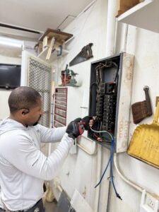 An electrician from Green Volt Electric LLC servicing an electrical panel inside a workshop in Durham, NC.