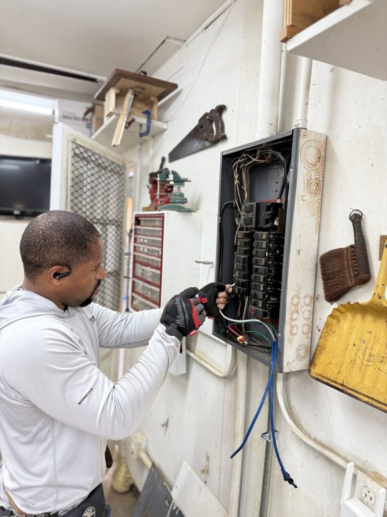 An electrician from Green Volt Electric LLC servicing an electrical panel inside a workshop in Durham, NC.