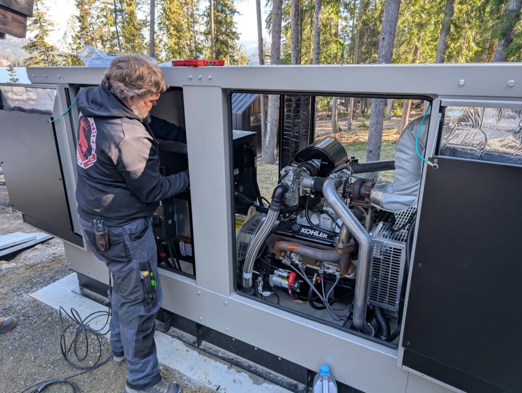 An electrician servicing the engine of an open Kohler generator for Great Northern Power in Kalispell, MT.