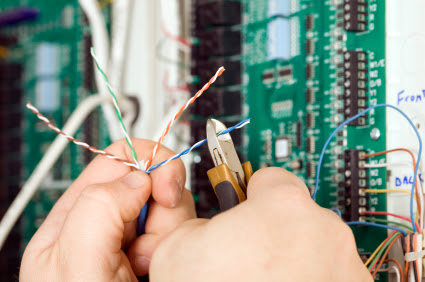 An electrician stripping wires near a circuit board for Agape Electric in Kenai, AK.