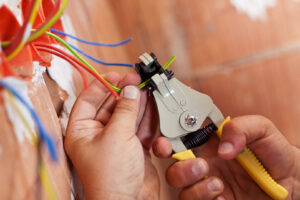 Close-up of an electrician's hands using a wire stripper on colored electrical wires, demonstrating work by Beaver Electric in Hillsboro, OR.