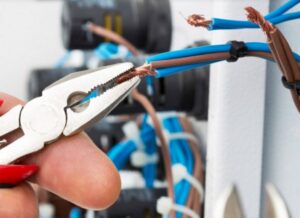 An electrician stripping electrical wires with pliers, performing detailed work for Devaney Electric Co. in Lacey, WA.