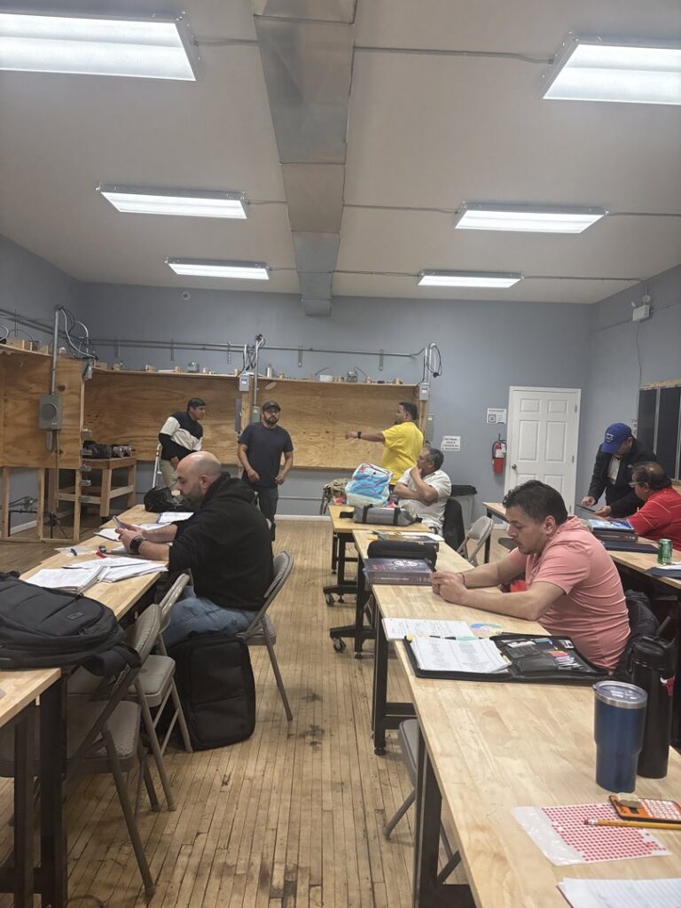 Electrician students attending a class with electrical training panels visible in the background at Escuela Tecnica ABC in North Chicago, IL