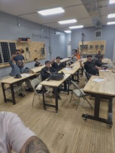 Electrician students giving thumbs up in a classroom with electrical and solar training panels in the background at Escuela Tecnica ABC in North Chicago, IL