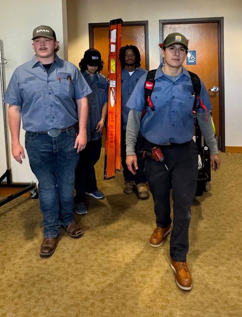 A team of electricians, one carrying a ladder, walking together for Three Rivers Electric in Fort Wayne, IN.