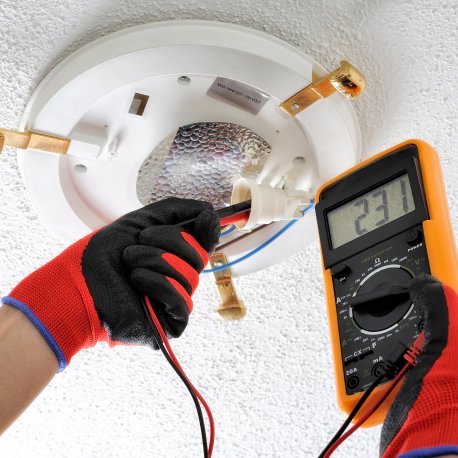 An electrician testing a ceiling light fixture with a multimeter for Illiana Electrical in Whiting, IN