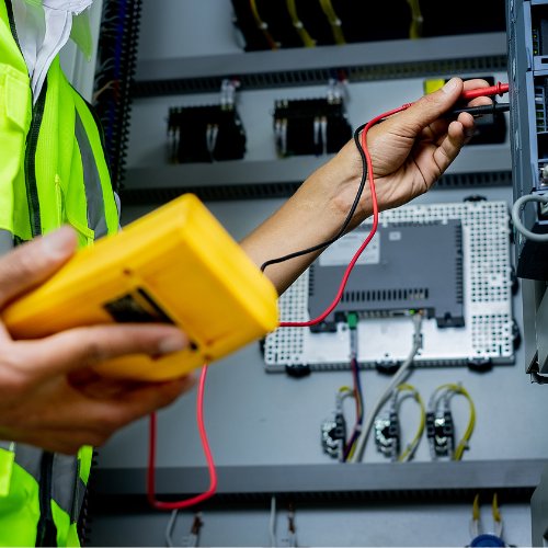 An electrician in a safety vest using a multimeter to test a circuit breaker panel for D. Geer Electric Inc. in Waukegan, IL.
