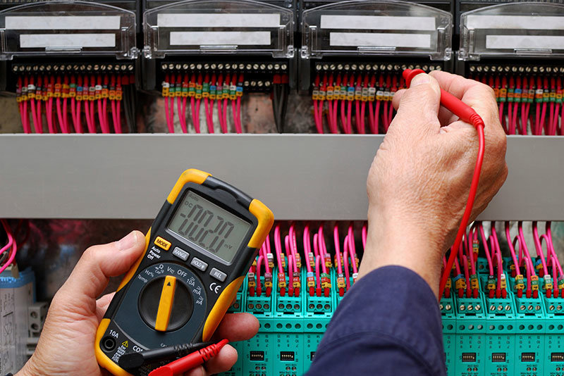 An electrician using a multimeter to test wiring in an electrical control panel for OMR Electrical Contractors Inc. in Cape Coral, FL.