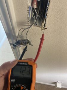 An electrician testing the voltage of an electrical outlet with a multimeter, performed by Outlaw Home Services, LLC in San Antonio, Tx.