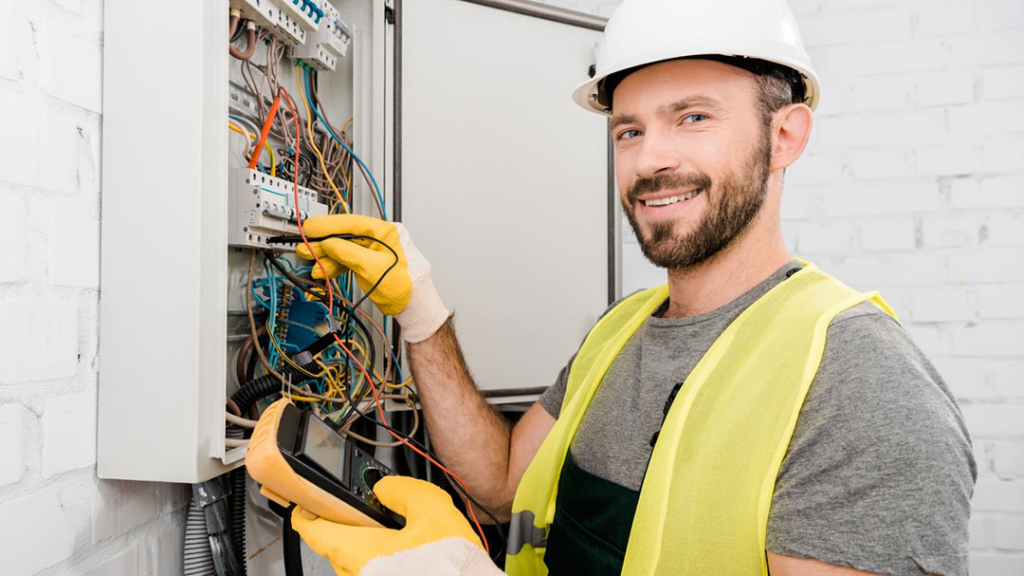 A smiling electrician testing an electrical panel with a multimeter for All American Pro Electric LLC in Cedar Creek, TX.