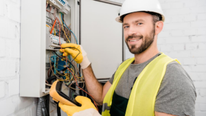 A smiling electrician testing an electrical panel with a multimeter for All American Pro Electric LLC in Cedar Creek, TX.