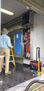 An electrician on a ladder testing an open electrical panel for F & L Electrical, LLC in Clemmons, NC.