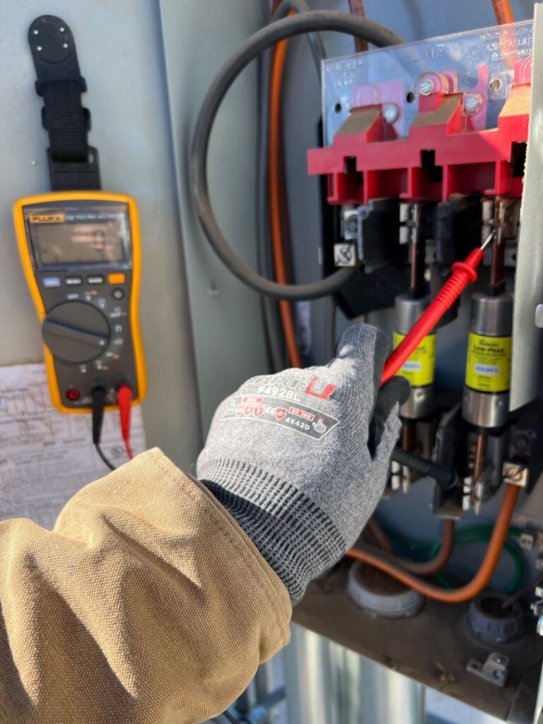An electrician from Sparrow Electric, LLC testing an outdoor electrical panel with a multimeter in Denver, CO.