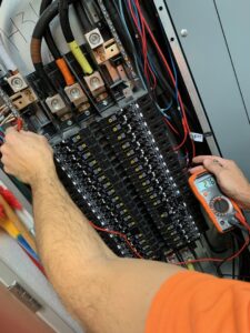 An electrician's hands using a multimeter to test an electrical panel, demonstrating diagnostic services by Volta Electrical LLC in Plano, TX.