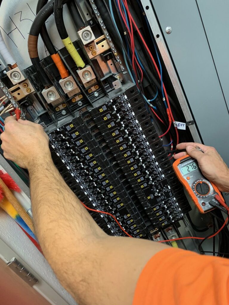 An electrician's hands using a multimeter to test an electrical panel, demonstrating diagnostic services by Volta Electrical LLC in Plano, TX.