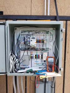 An electrician testing an outdoor electrical control panel with a multimeter for J&L Electric Inc. in San Antonio, TX