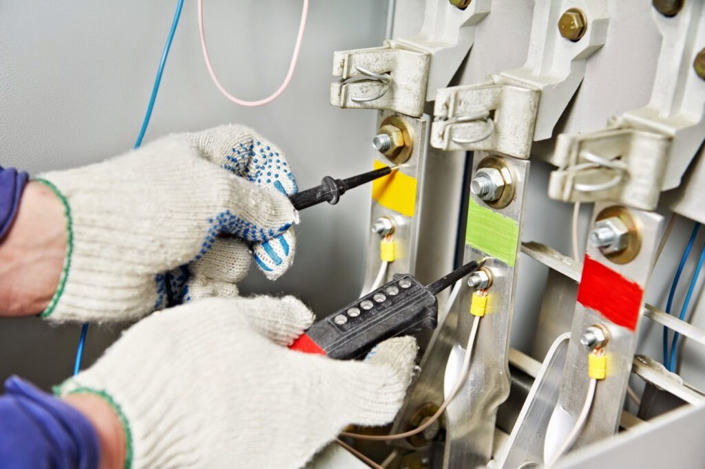 An electrician in gloves using a multimeter to test electrical components in a panel for Reliable Electric in Olympia, WA.