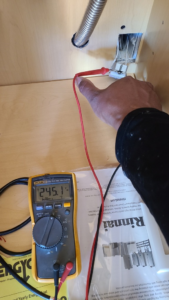 An electrician using a multimeter to test voltage, showing 245.1V, performed by AnchorLine Electrical in Alaska, AK