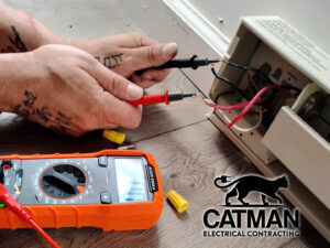 An electrician's hands using a multimeter to test electrical wiring, performed by Catman Electrical Contracting in Dallas, PA.