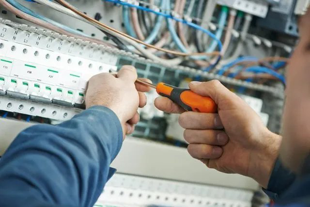 An electrician using a screwdriver to tighten connections on a row of circuit breakers for Joe Chick A/C & Electric in Zapata, TX