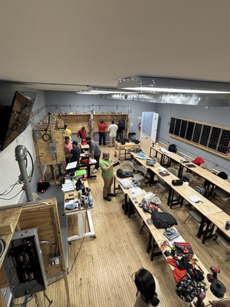 An overhead view of an electrician training workshop with students working on electrical and solar panels at Escuela Tecnica ABC in North Chicago, IL