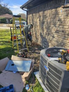 An electrician using a jackhammer for trenching near an outdoor AC unit and electrical panel in Plano, TX, by Tesla Alarm and Electrical