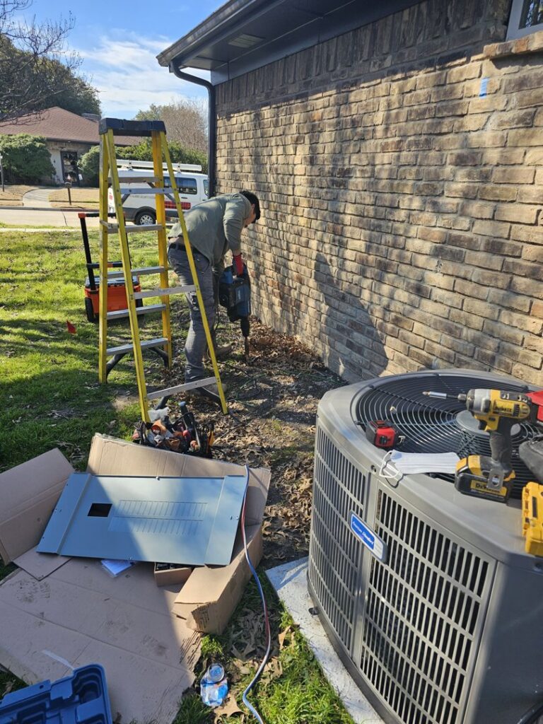 An electrician using a jackhammer for trenching near an outdoor AC unit and electrical panel in Plano, TX, by Tesla Alarm and Electrical