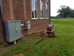 An electrician operating a trencher near outdoor electrical panels at a job site for Visual Electric, Inc. in Frederick, MD.