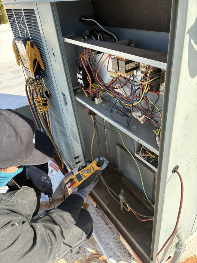 An electrician using a clamp meter to check electrical current in an HVAC unit for Cool Aid Air Conditioning in Scottsdale, AZ.