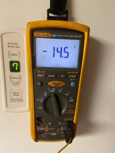 An electrician using a Fluke multimeter for diagnostics, showing a temperature reading, by T.S.F Electric in Saco, ME.