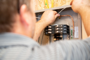 An electrician wiring a breaker box, connecting wires to circuit breakers for Jarvie Electric in Rochester, NY.