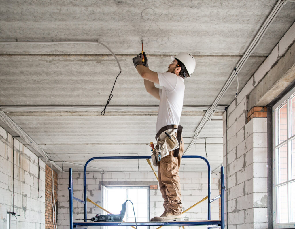 An electrician on scaffolding installing electrical wiring in a ceiling at a construction site, by Beaver Electric in Hillsboro, OR.