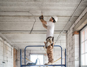 An electrician on scaffolding installing electrical wiring in a ceiling at a construction site, by Beaver Electric in Hillsboro, OR.