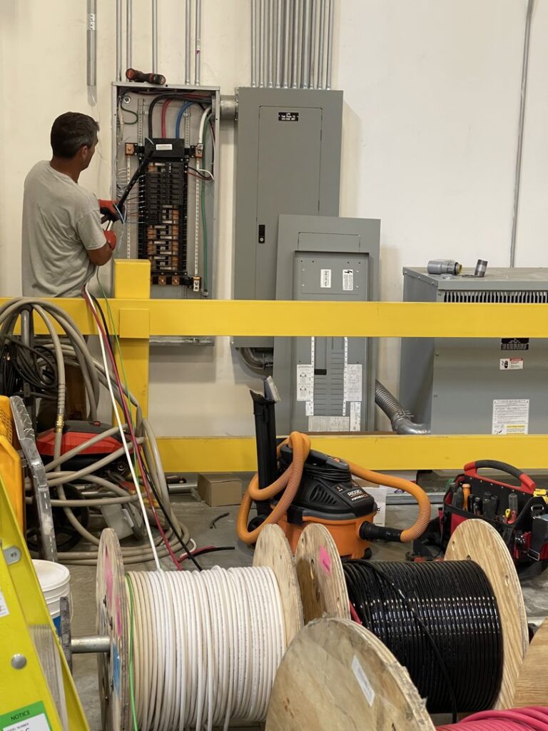 An electrician wiring a large commercial electrical panel with spools of wire in the foreground for Flowers Electric in Aurora, CO.