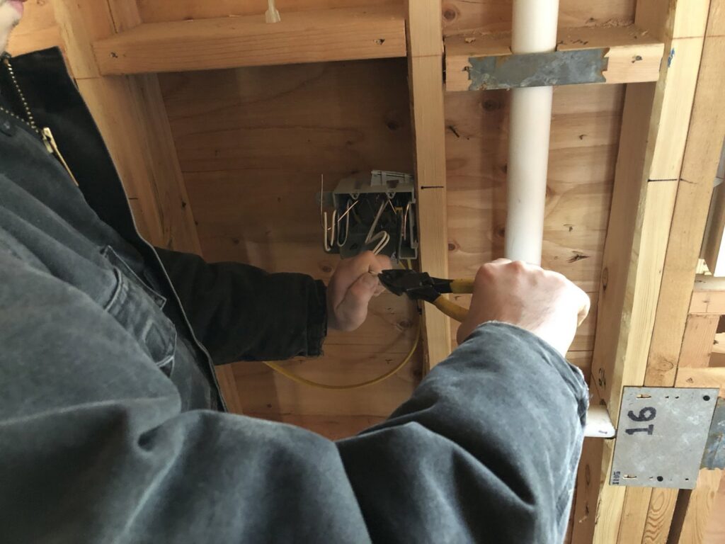 An electrician from Barrios Electric LLC wiring an electrical box in a framed wall in Norwalk, CT.