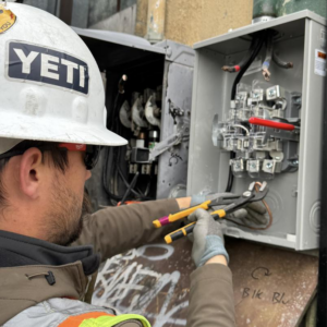 A close-up of an electrician in gloves using pliers to work on wiring inside an electrical panel for Wheeler Electric, Inc. in Idaho Falls, ID.