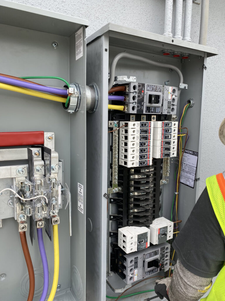 An electrician from Ultralight Electric wiring a main electrical panel with colorful wires and breakers in Houston, TX.